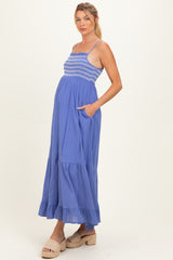 woman wearing a blue maternity maxi dress with smocking and pockets, showing her baby bump