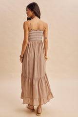 woman wearing a back view of a beige maxi dress with smocked bodice and tiered ruffle hem