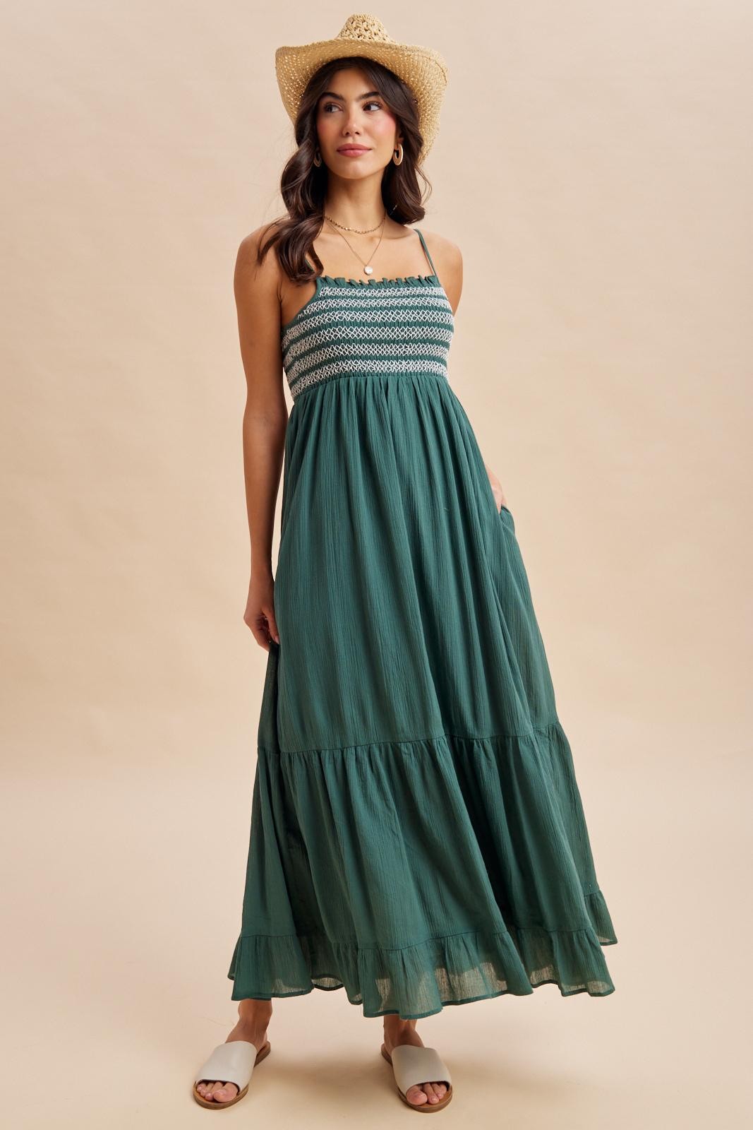 woman wearing a green maxi dress with a smocked bodice and tiered skirt, paired with a straw hat and slide sandals