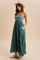 woman wearing a teal maxi dress with smocked bodice and tiered skirt, complemented by a straw hat and sandals