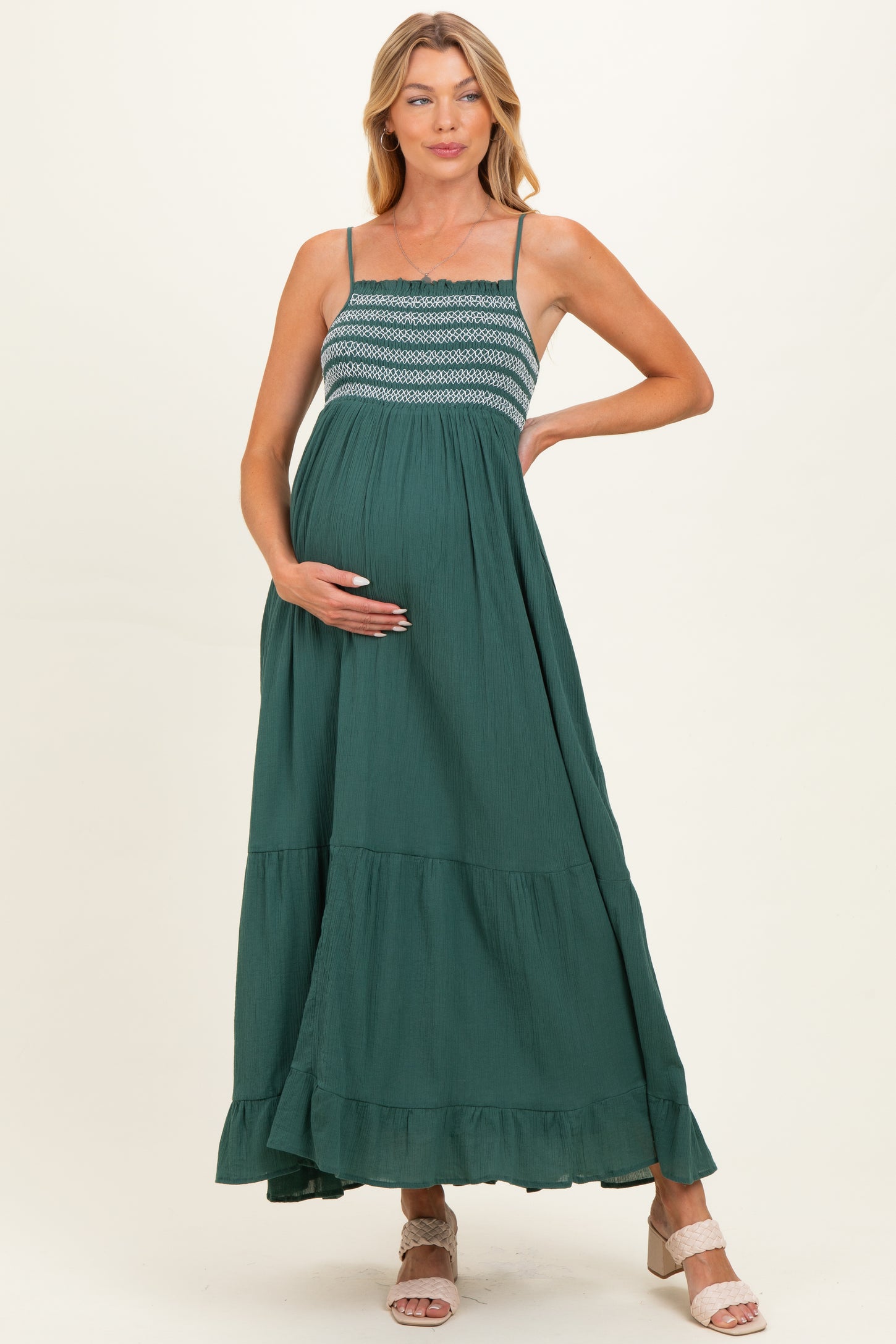 woman wearing a dark green maternity maxi dress with a smocked bodice and tiered skirt, holding her baby bump