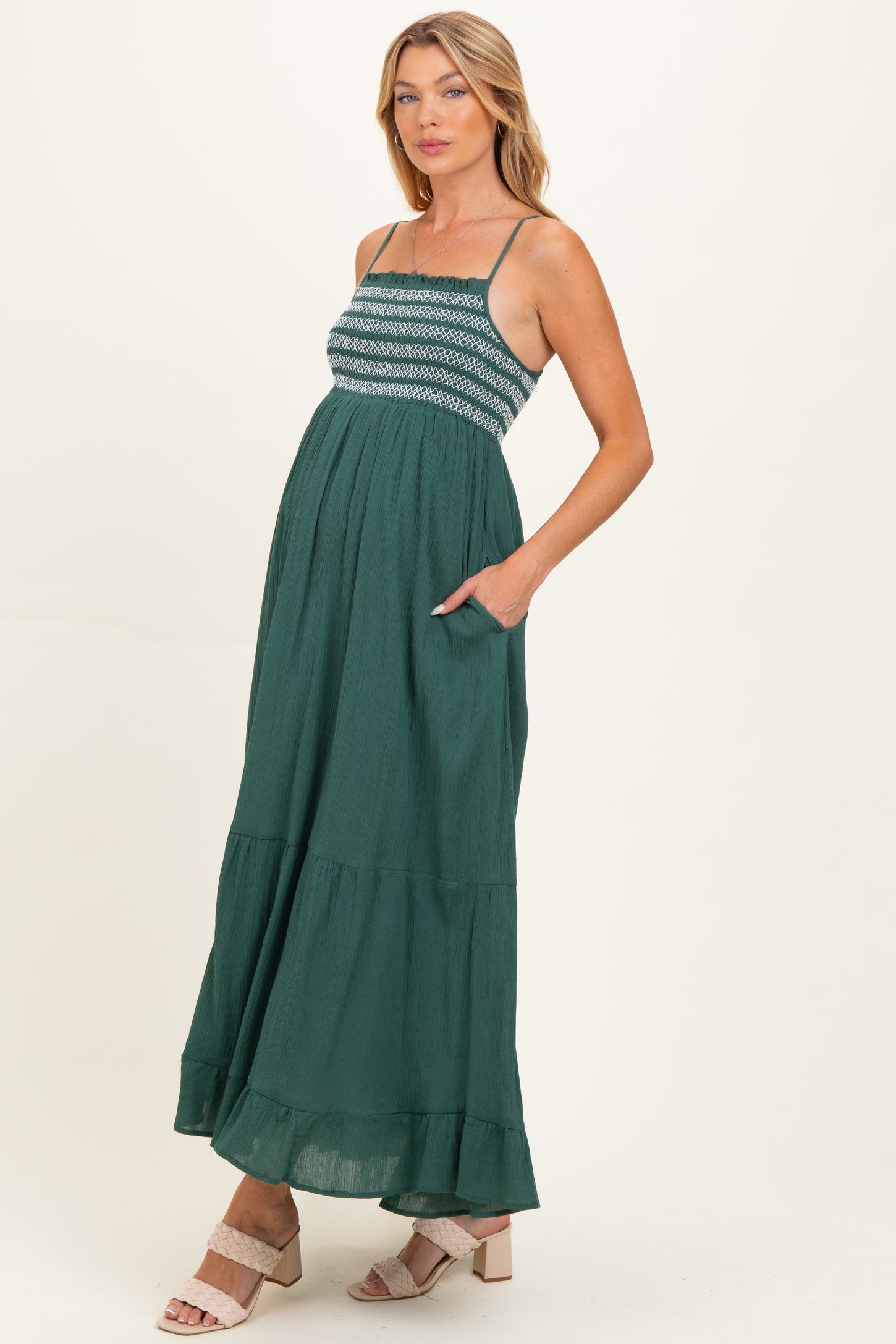 woman wearing a teal maternity maxi dress with a smocked bodice and pockets, showcasing her baby bump