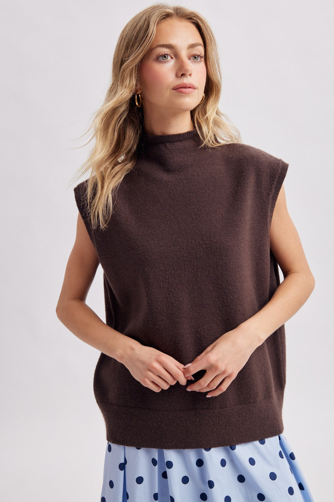 woman wearing a brown sleeveless mock neck sweater styled over a blue polka dot skirt