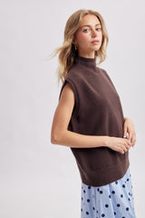 woman wearing a brown sleeveless turtleneck sweater paired with a blue polka dot skirt