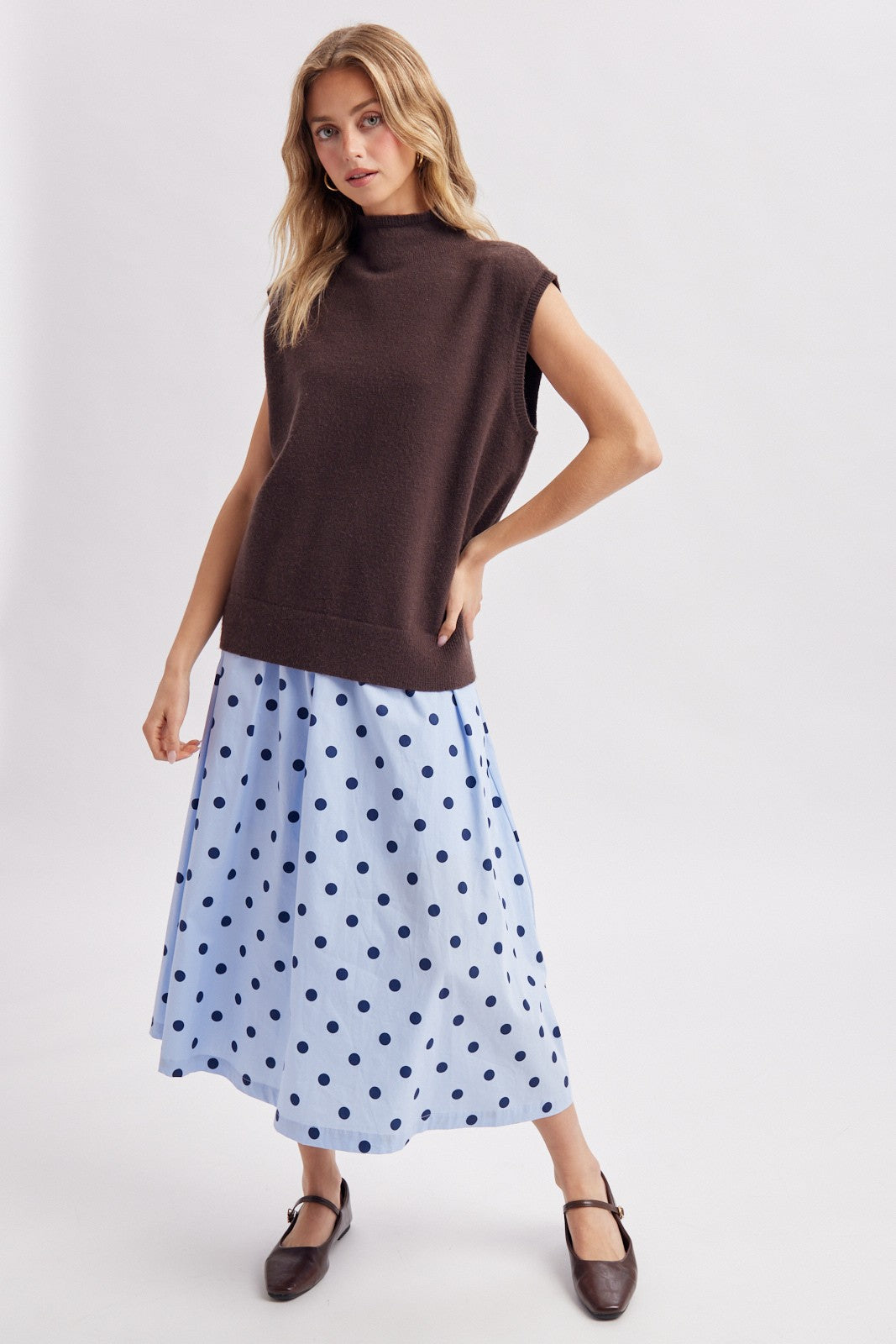 woman wearing a brown sleeveless sweater and a light blue polka dot skirt with ankle strap flats