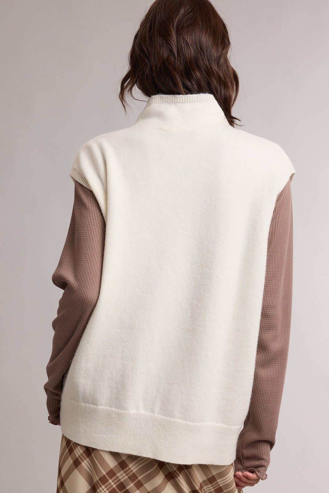 woman wearing a cream-colored sleeveless sweater with brown long sleeves layered underneath