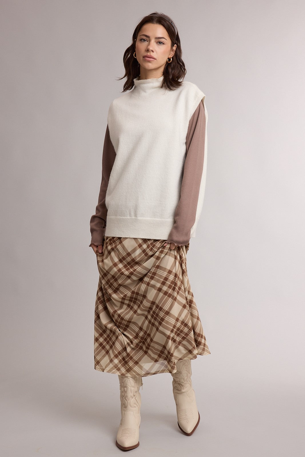 woman wearing a cream oversized sweater with brown sleeves and a plaid midi skirt paired with cream ankle boots