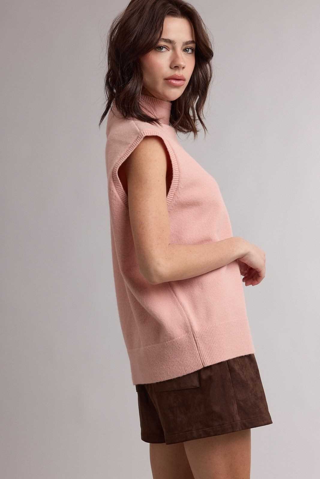 woman wearing a pink sleeveless turtleneck sweater paired with brown suede shorts
