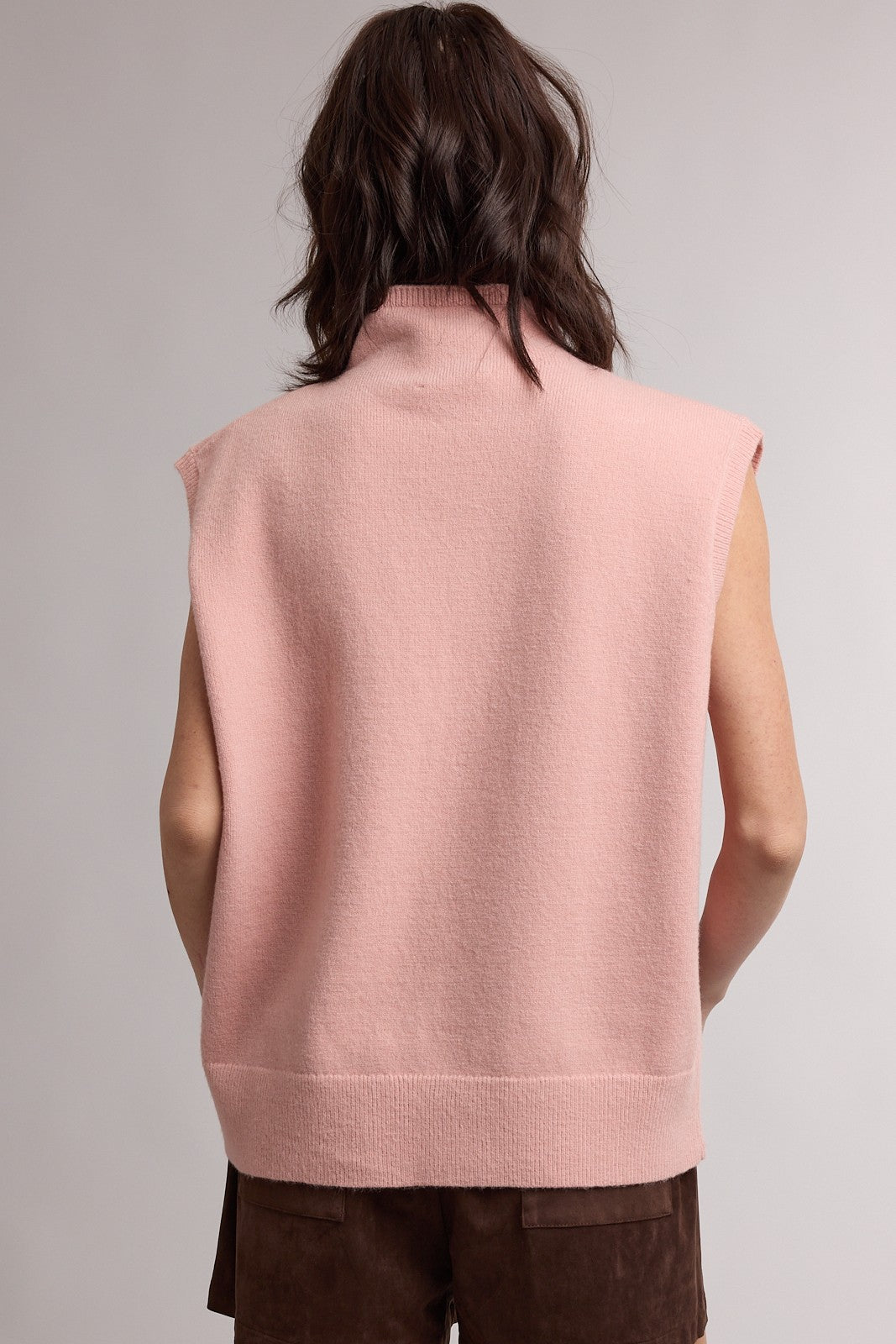 woman wearing a soft pink sleeveless turtleneck sweater with a relaxed fit, viewed from the back