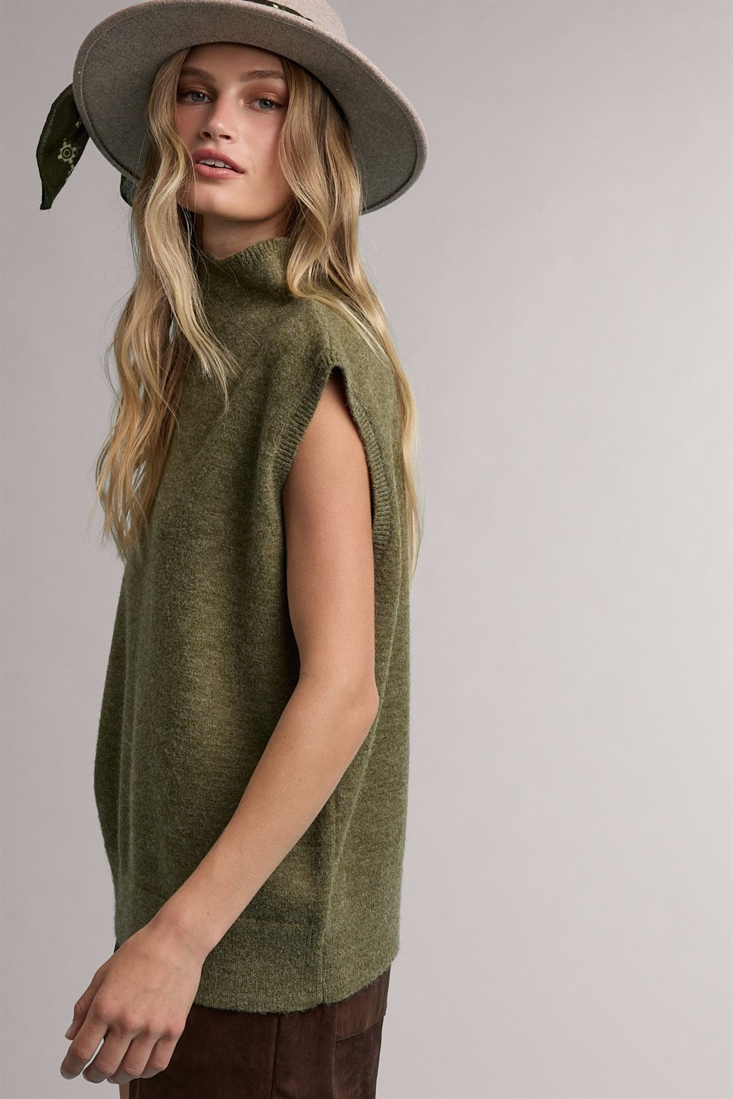 woman wearing a green sleeveless turtleneck sweater and a wide-brimmed hat