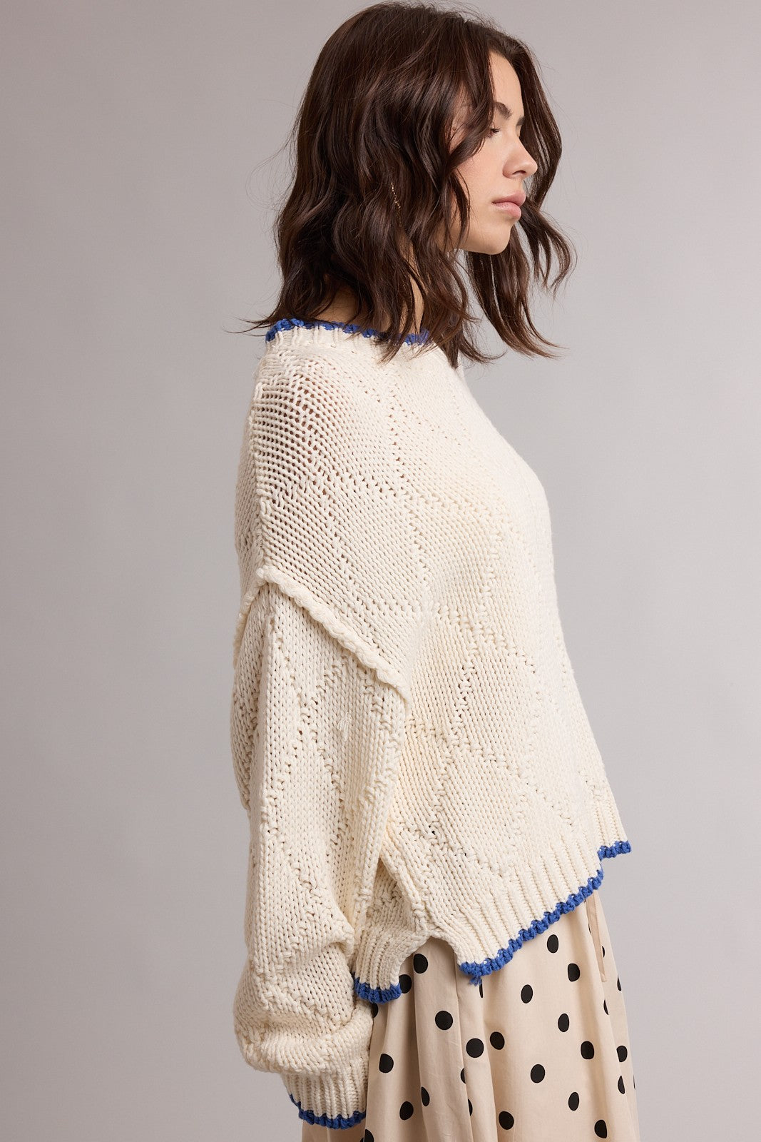 woman wearing a cream colored knitted sweater with blue trim and a loose fit, paired with a polka dot skirt