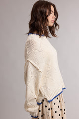 woman wearing a cream colored knitted sweater with blue trim and a loose fit, paired with a polka dot skirt