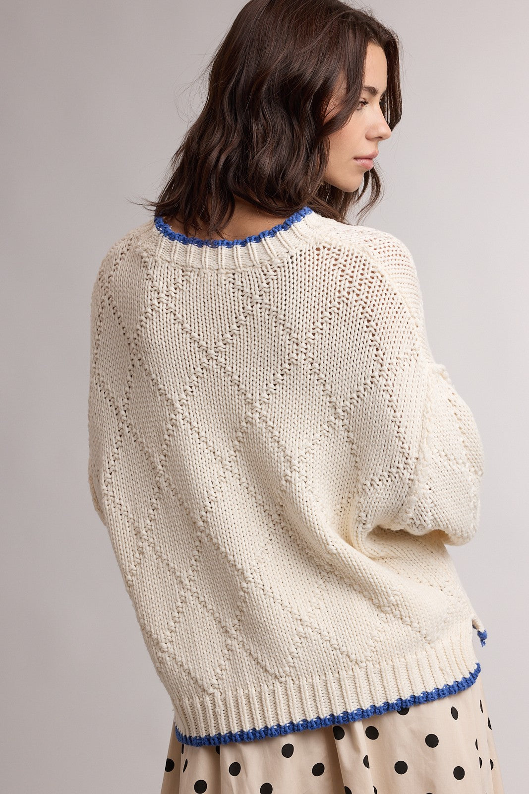 woman wearing an ivory oversized knitted sweater with diamond pattern and blue detailing on the neckline and hem