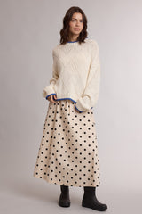 woman wearing a cream sweater with blue trim and a beige polka dot maxi skirt, paired with black ankle boots