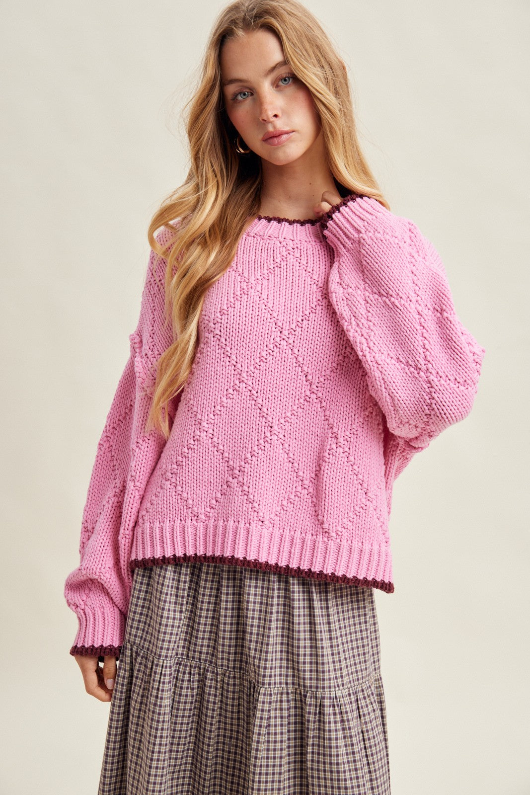 woman wearing a pink oversized knitted sweater with diamond pattern and a gray plaid skirt