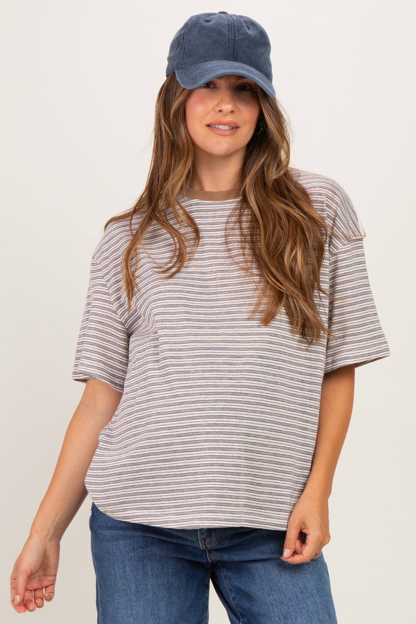woman wearing a striped oversized maternity top and a navy baseball cap, with a slight baby bump visible