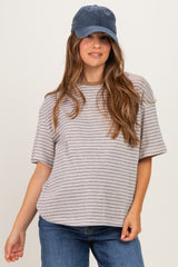 woman wearing a striped oversized maternity top and a navy baseball cap, with a slight baby bump visible