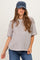 woman wearing a striped oversized maternity top and a navy baseball cap, with a slight baby bump visible