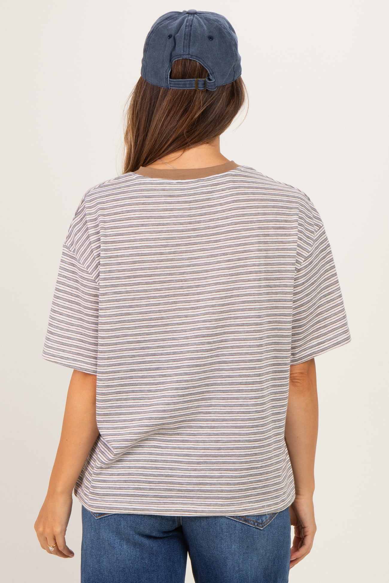 woman wearing a striped gray and white oversized maternity t-shirt and a blue baseball cap