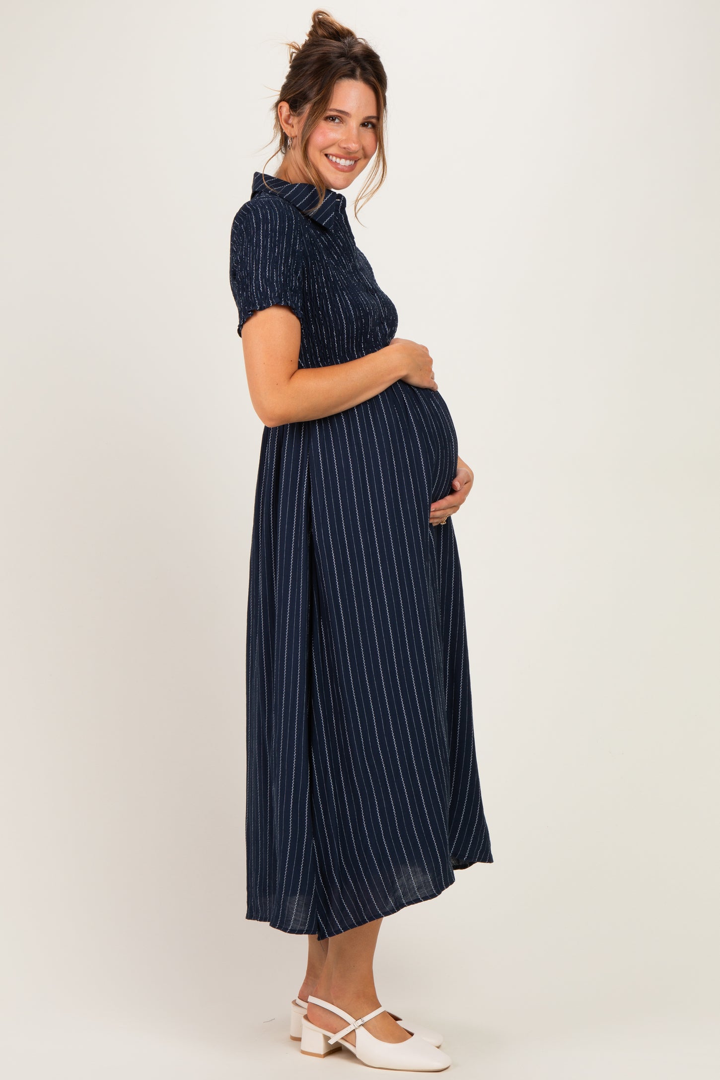 woman wearing a navy blue striped maternity dress with a fitted bodice, holding her baby bump and smiling