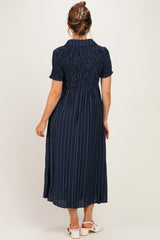 woman wearing a navy blue striped maternity dress with short sleeves and a smocked bodice, showing off her baby bump