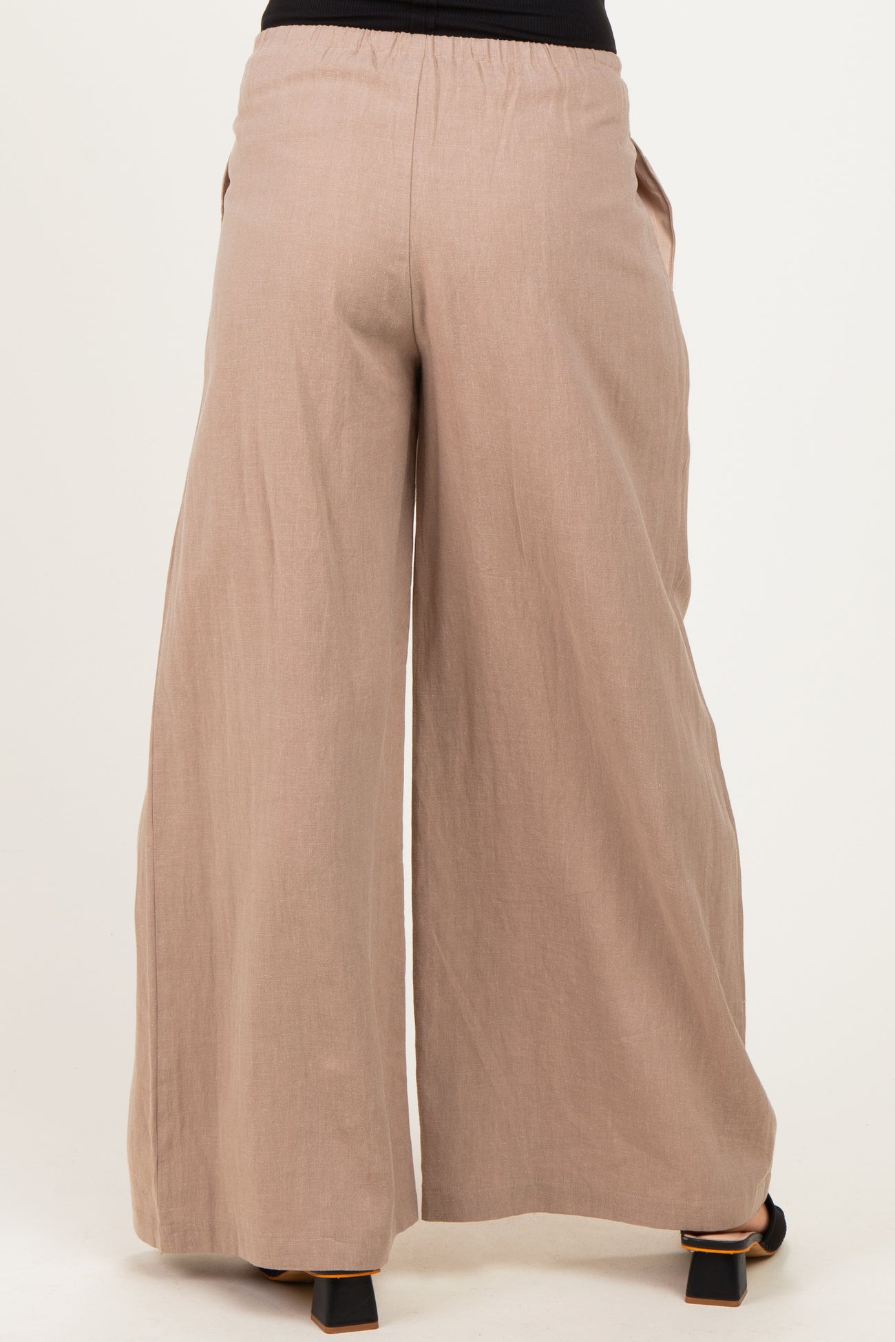 woman wearing light brown wide leg maternity pants with an elastic waistband and side pockets, viewed from the back
