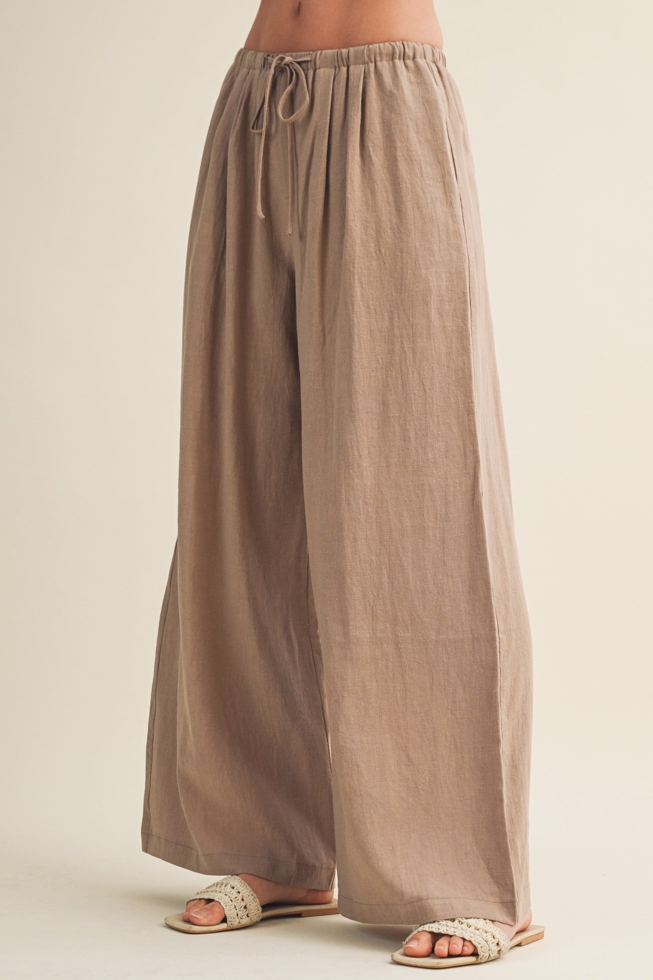 woman wearing beige wide-leg linen pants with an elastic waistband and drawstring detail