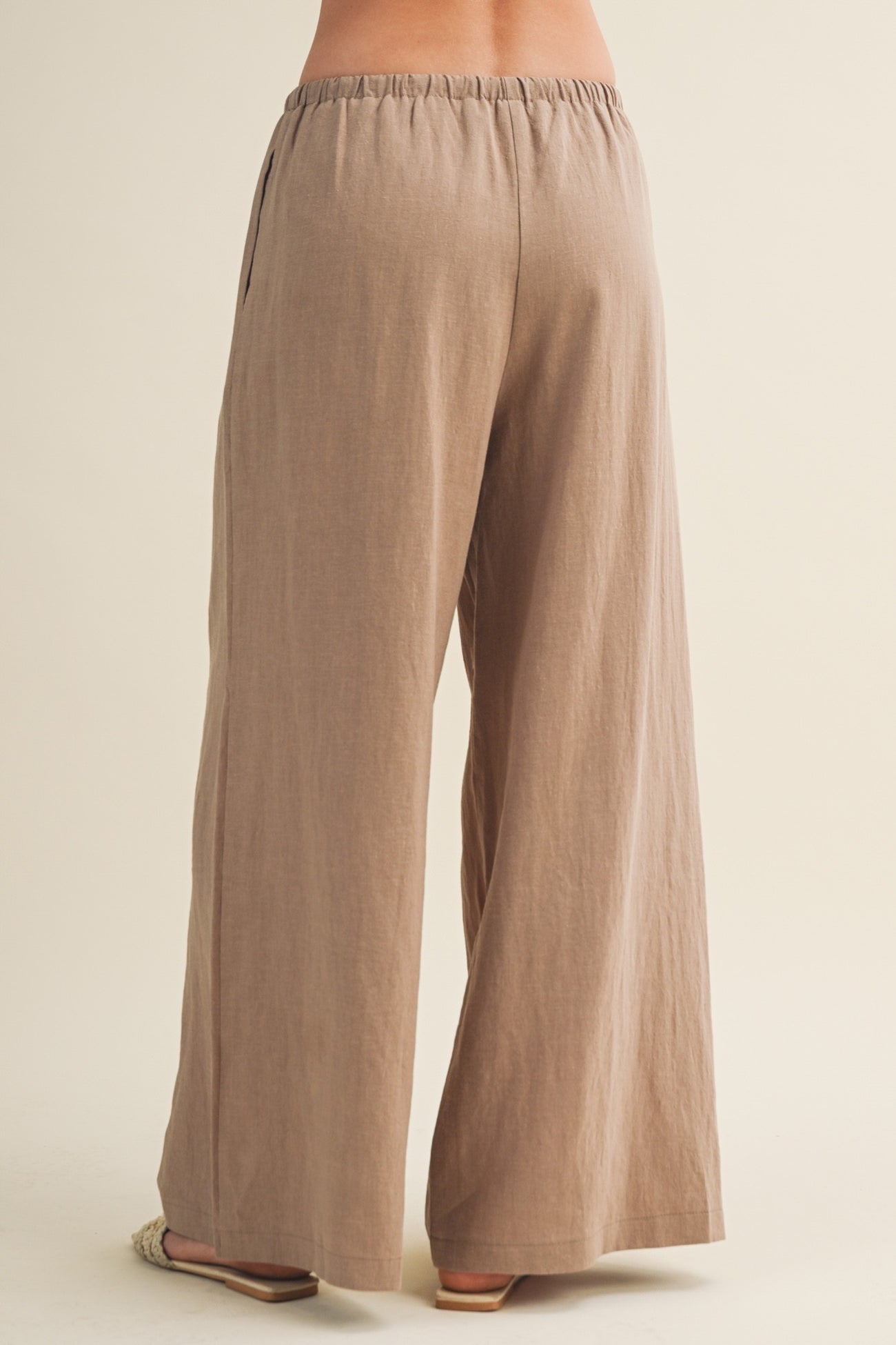 woman wearing light brown wide-leg pants with an elastic waistband, shown from the back