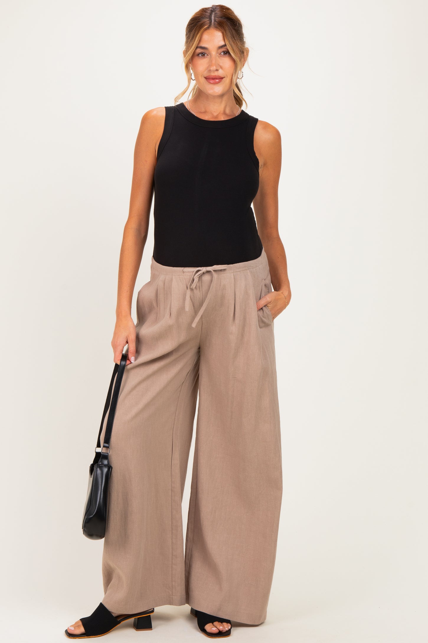 woman wearing a fitted black maternity tank top and wide-leg beige maternity pants with pockets