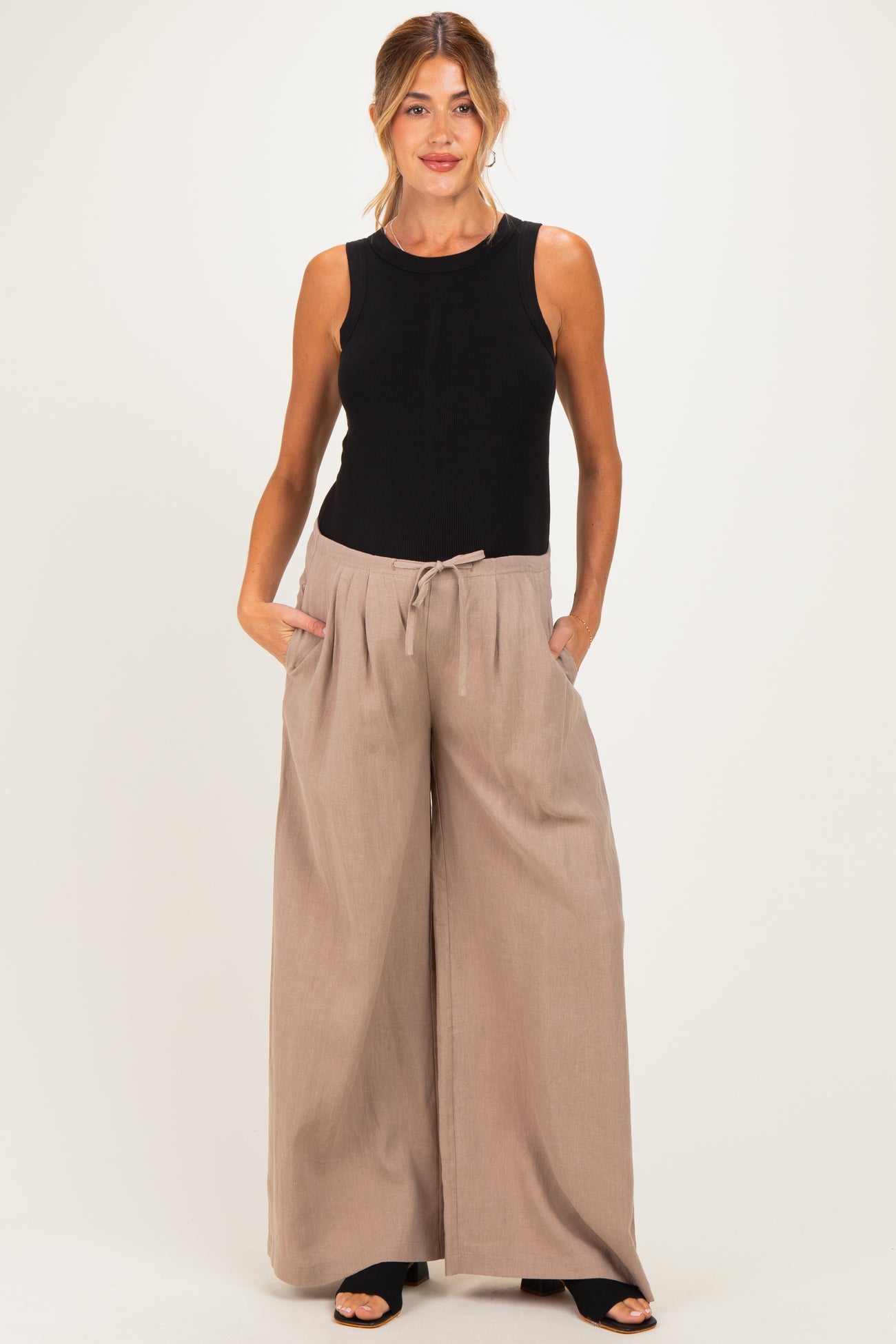 woman wearing a black sleeveless maternity top and beige wide-leg maternity pants with pockets