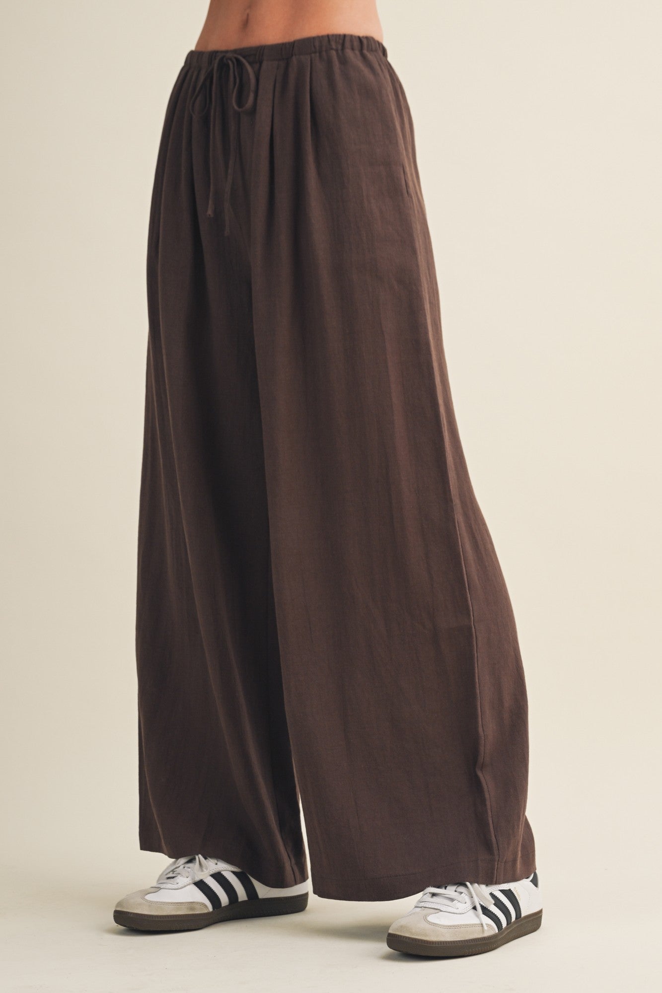 woman wearing brown wide-leg pants with an elastic waistband and drawstring, paired with white and black sneakers