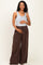 woman wearing a gray ribbed maternity tank top and brown wide-leg maternity pants, holding her baby bump
