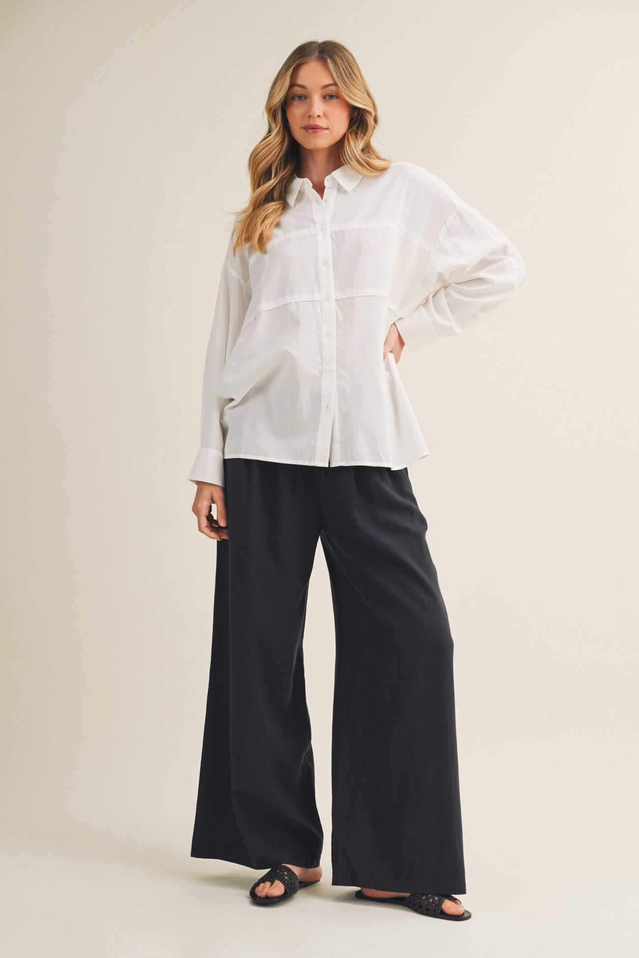 woman wearing a white button-up shirt and black wide-leg pants standing against a neutral background