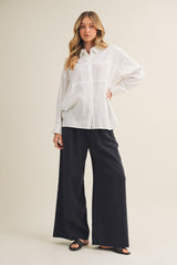 woman wearing a white button-up shirt and black wide-leg pants standing against a neutral background