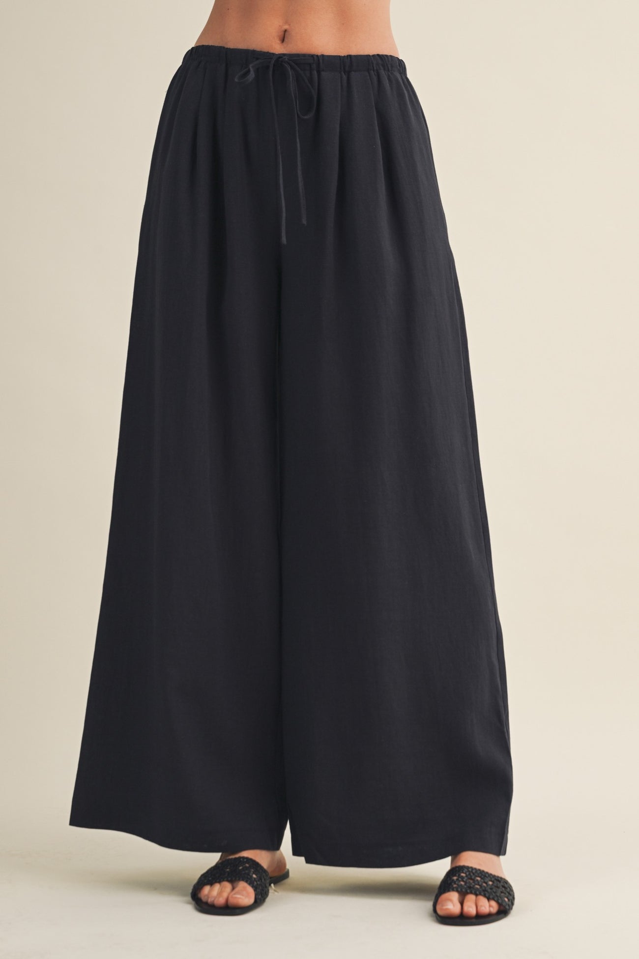 woman wearing black wide-leg trousers with an elastic waistband and drawstring, paired with open-toed black sandals