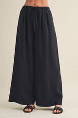 woman wearing black wide-leg trousers with an elastic waistband and drawstring, paired with open-toed black sandals