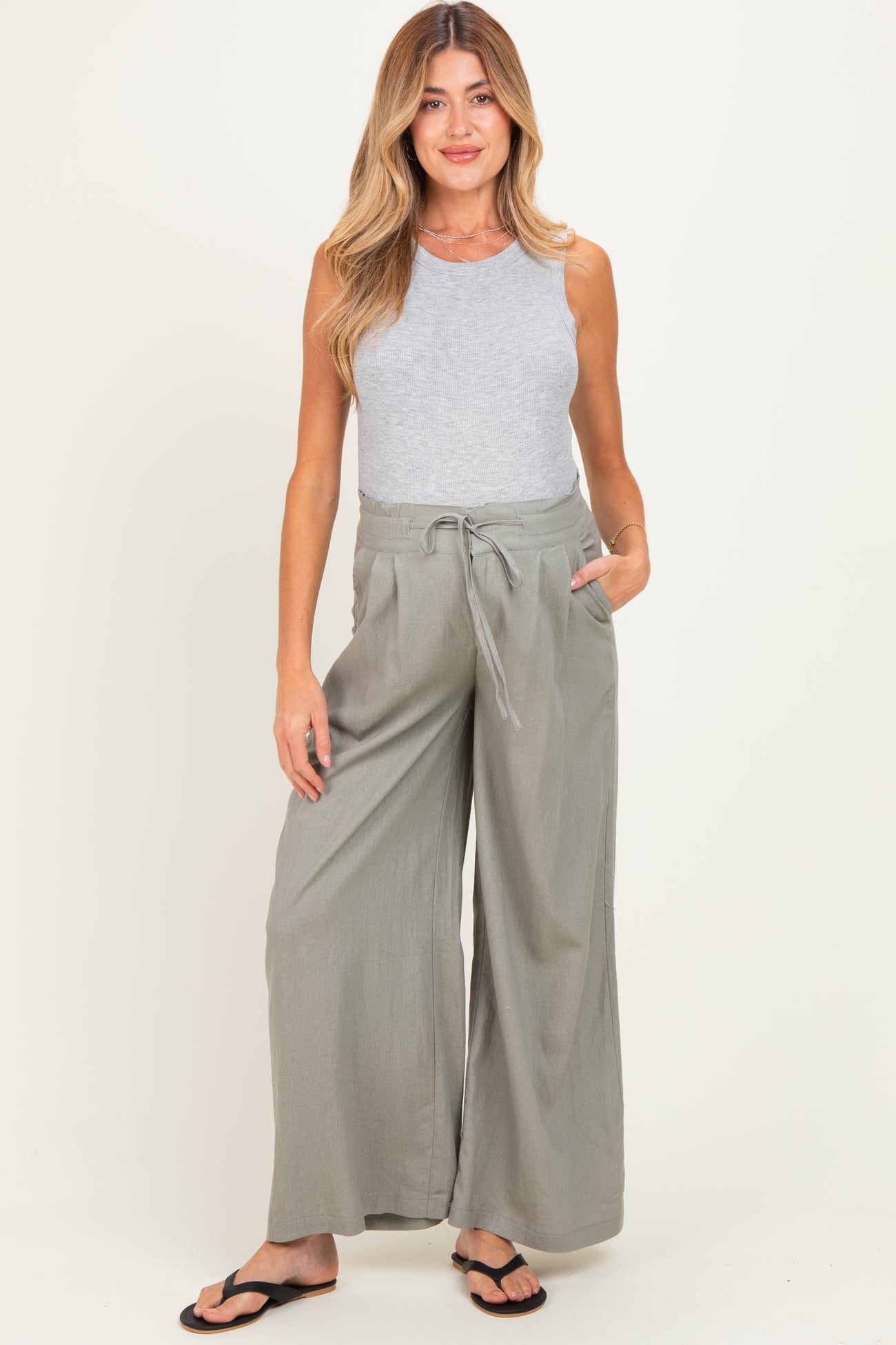 woman wearing a gray sleeveless top and light gray wide-leg maternity pants with pockets and a drawstring waist