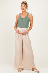 woman wearing a green plaid maternity tank top and beige wide-leg pants, holding her baby bump