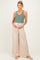 woman wearing a green plaid maternity tank top and beige wide-leg pants, holding her baby bump