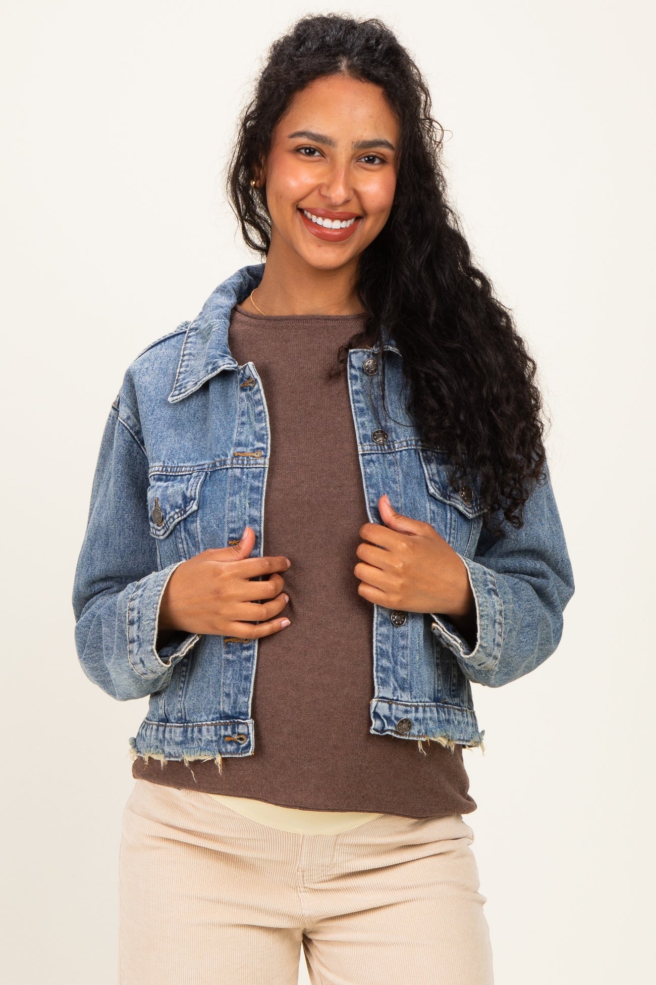 woman wearing a light blue denim maternity jacket over a brown top, smiling at the camera
