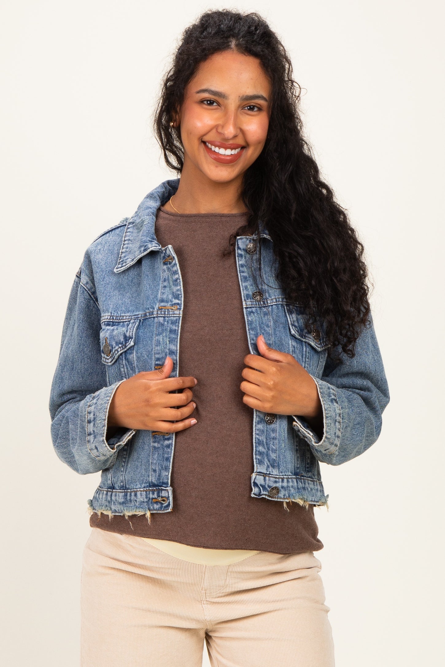 woman wearing a light blue denim maternity jacket over a brown top, smiling at the camera