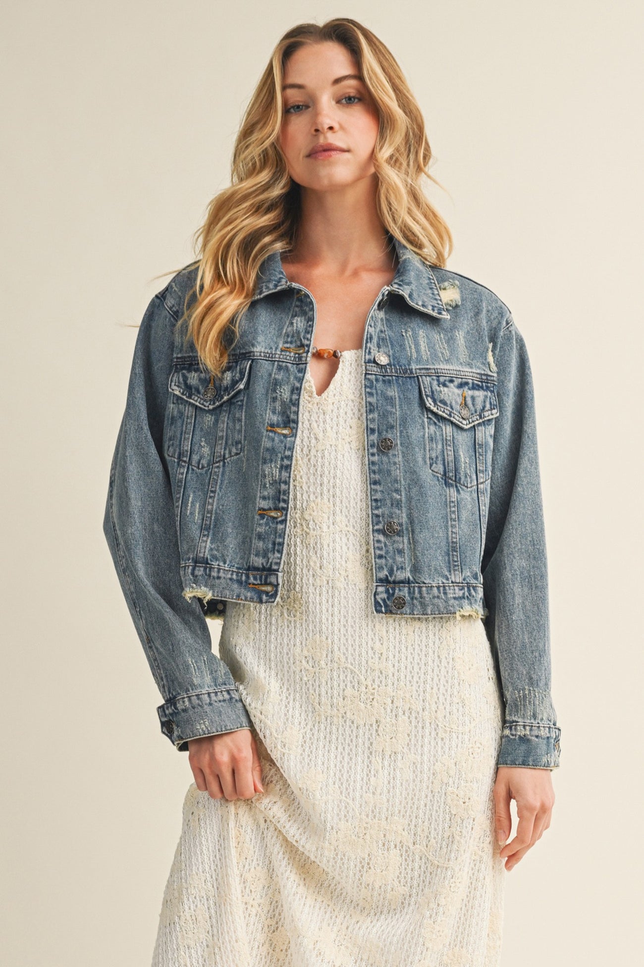 woman wearing a distressed light blue cropped denim jacket over a white maxi dress