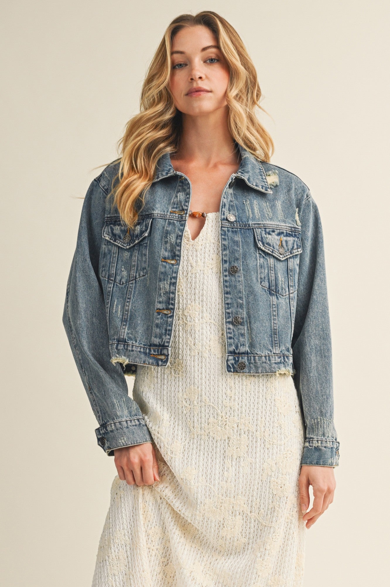 woman wearing a distressed light blue cropped denim jacket over a white maxi dress