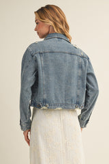 woman wearing a distressed denim jacket with a cropped cut, styled over a lace dress, showing the back view