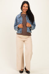 woman wearing a denim jacket over a brown top and beige wide-leg pants, showcasing a visible baby bump in maternity wear