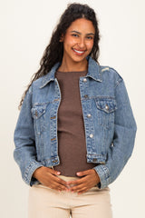 woman wearing a light blue maternity denim jacket over a brown top, gently holding her baby bump