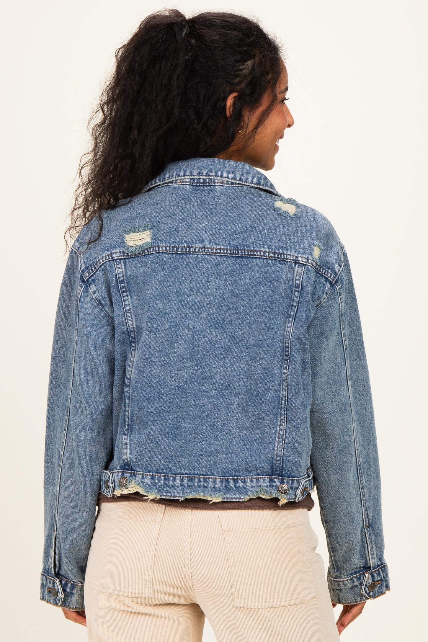 woman wearing a distressed light blue denim jacket, showcasing a relaxed fit and frayed hem, seen from the back