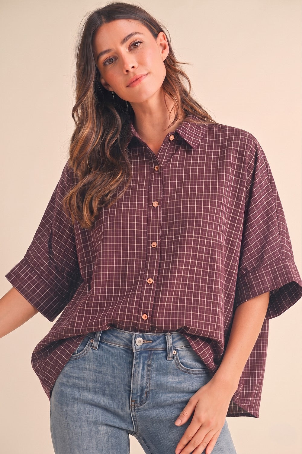 woman wearing a burgundy and white checkered oversized button-up shirt with short sleeves and light blue jeans