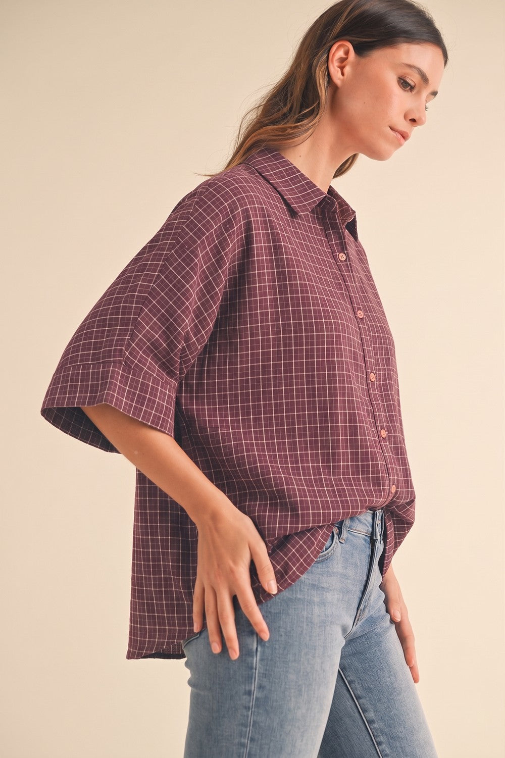 woman wearing a maroon checkered oversized button-up shirt with relaxed sleeves and paired with light blue jeans