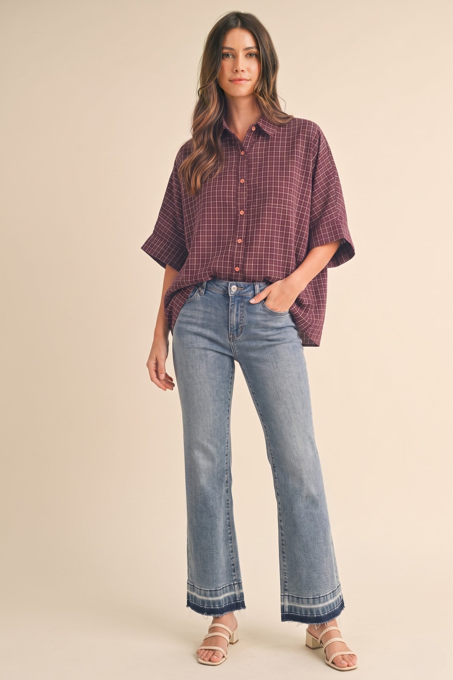 woman wearing a burgundy checkered oversized button-up shirt and light blue flared jeans with a hem detail